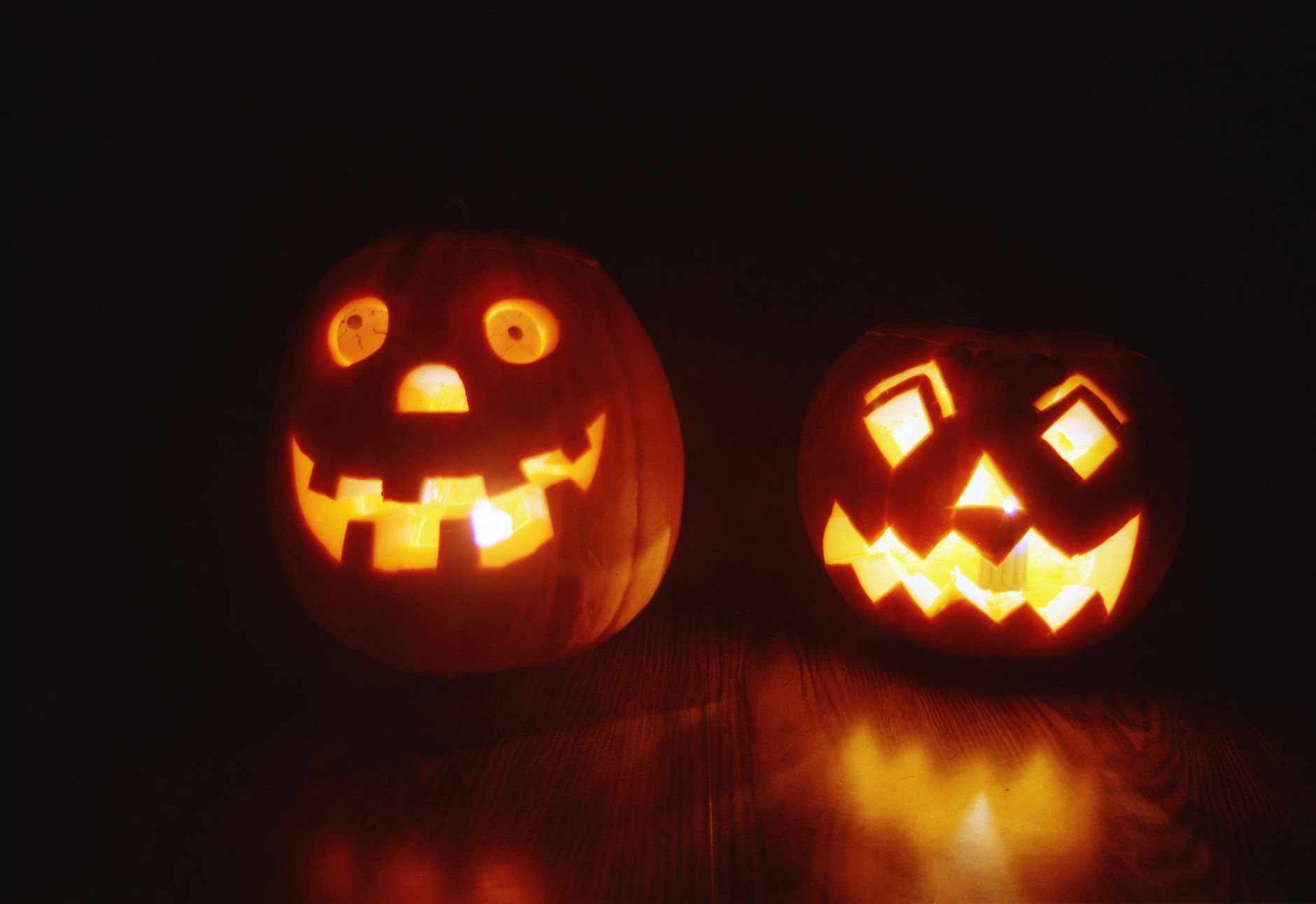 Deux citrouilles d'Halloween sculptées, éclairées de l'intérieur et posées sur un plancher en bois dans le noir