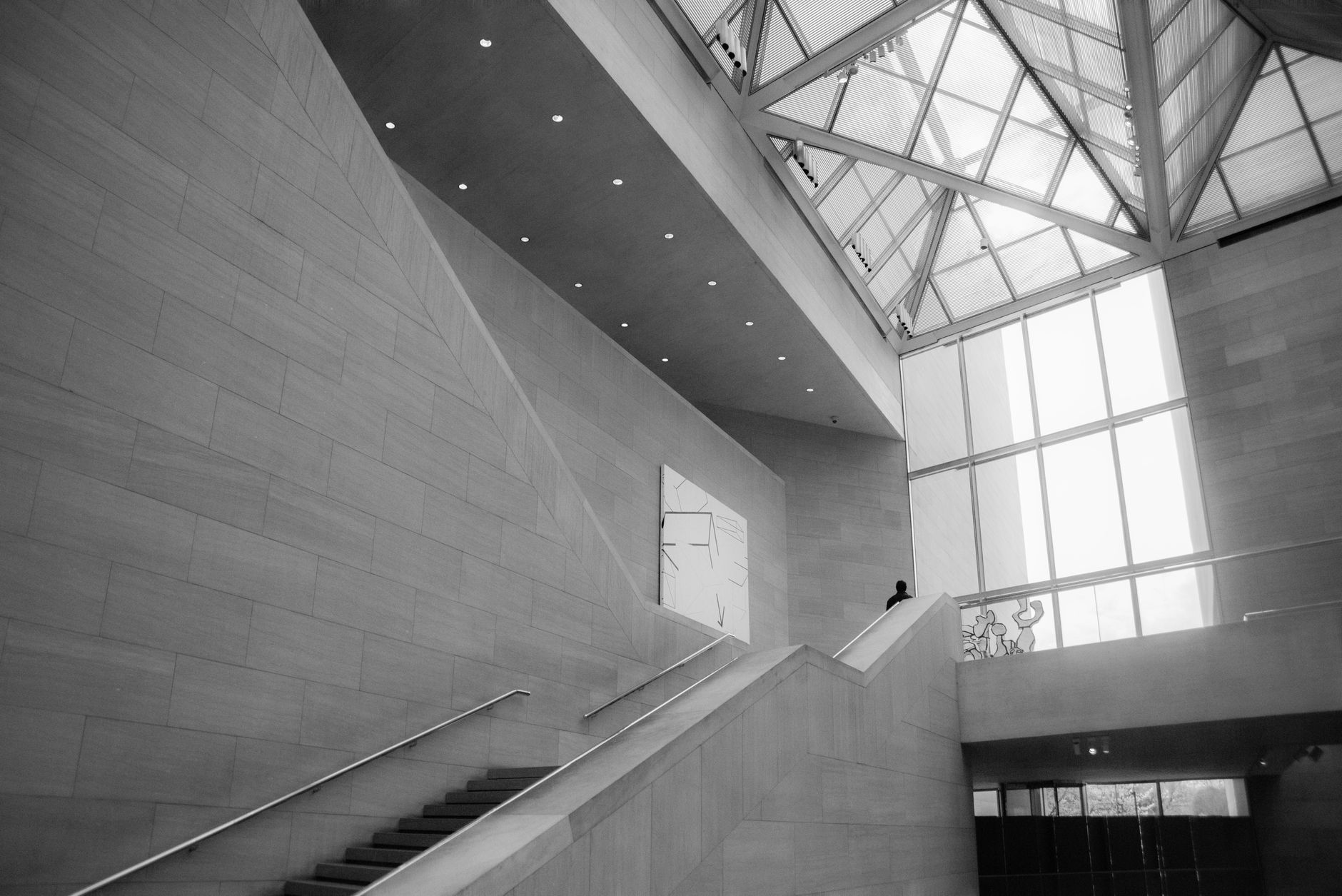 Vue intérieure monochrome d'une architecture moderne au design minimaliste, avec un puits de lumière en verre et un escalier montant.