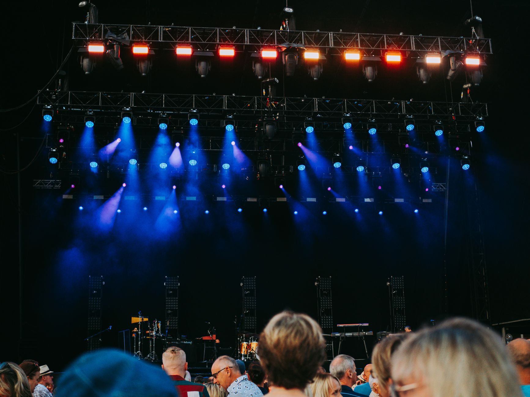 Public de dos devant une scène de concert éclairée de projecteurs bleus et orange